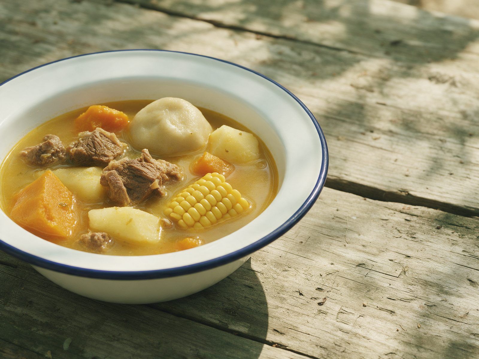A big bowl of beef soup with pumpkin, yam, a dumpling and corn on the cob.